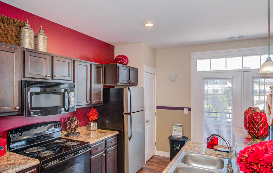 Ovens give off a lot of unwanted heat. Stick with slow cookers and deli-style food. A dark cabinet kitchen with red walls facing the oven and sink.